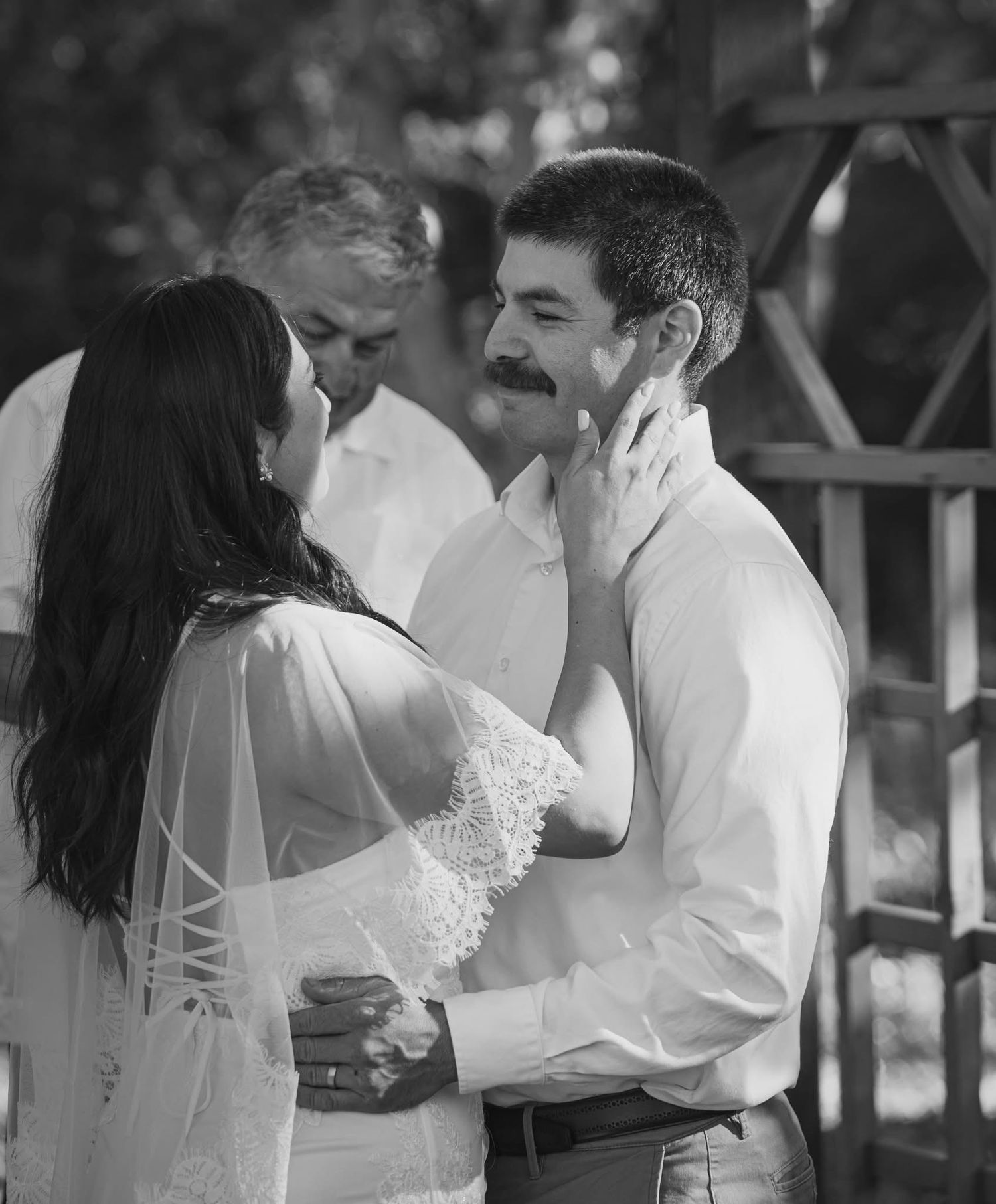 Black and white wedding photo of bride and groom sharing a tender moment, with officiant standing behind them.