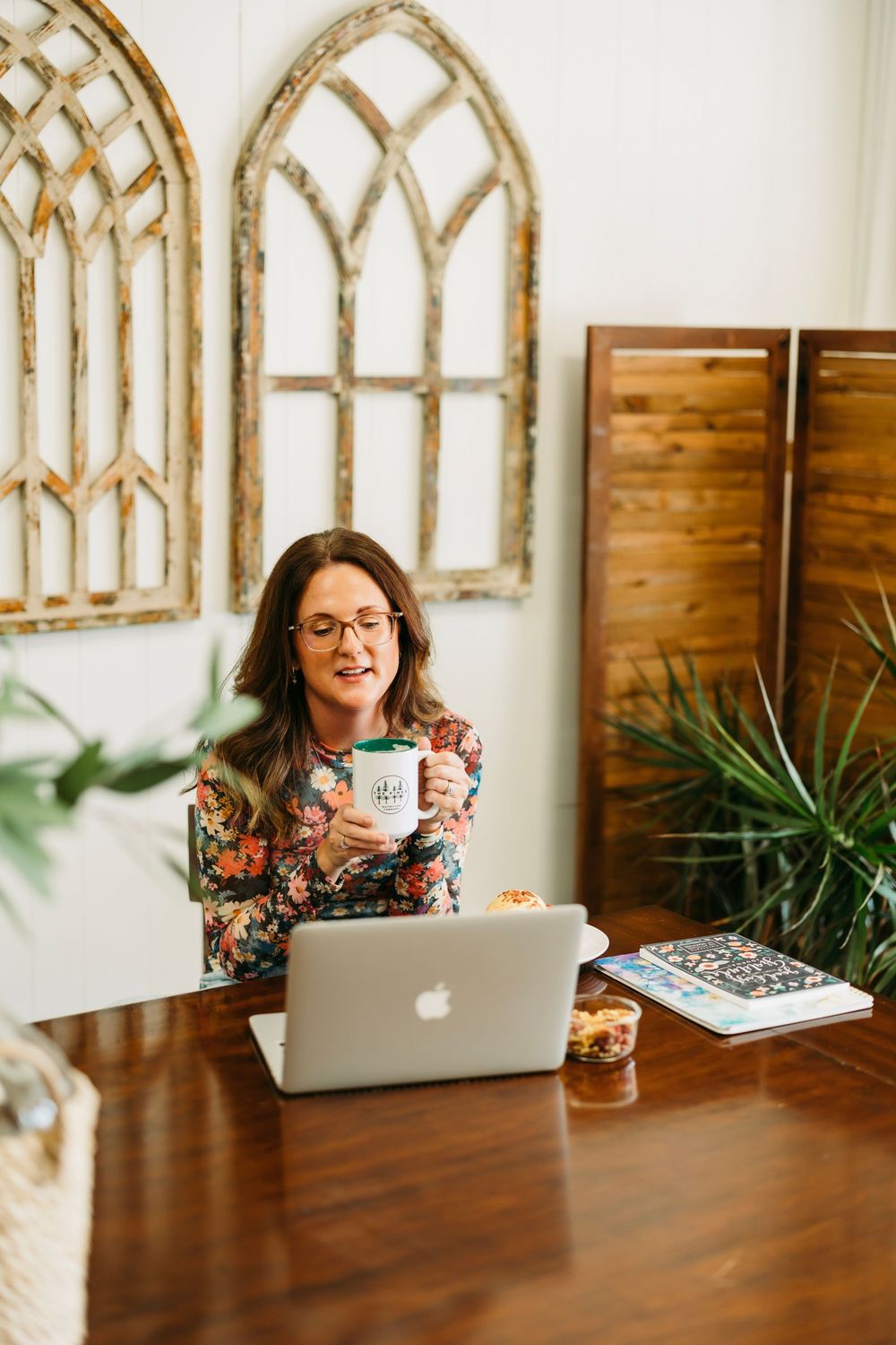 Someone working at a wooden desk with decorative arched wall decor and plants in a bright, modern office space.
