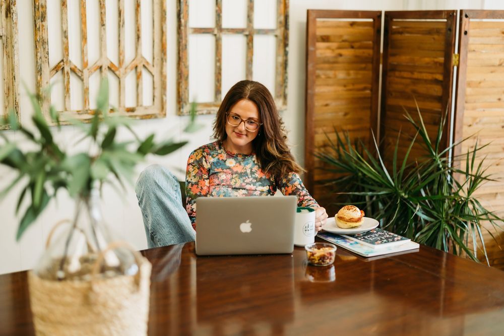 Someone works remotely from a wooden table with a laptop, plants and natural decor in a bright home office setting.