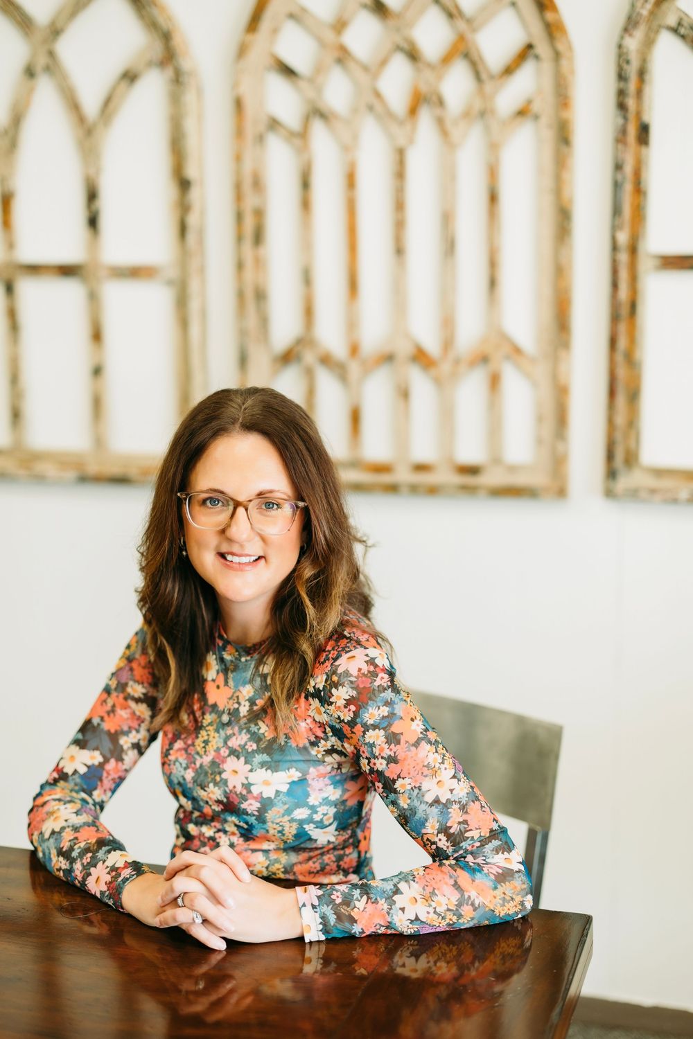 Professional headshots of someone in a floral top sitting at a desk in a bright office space.