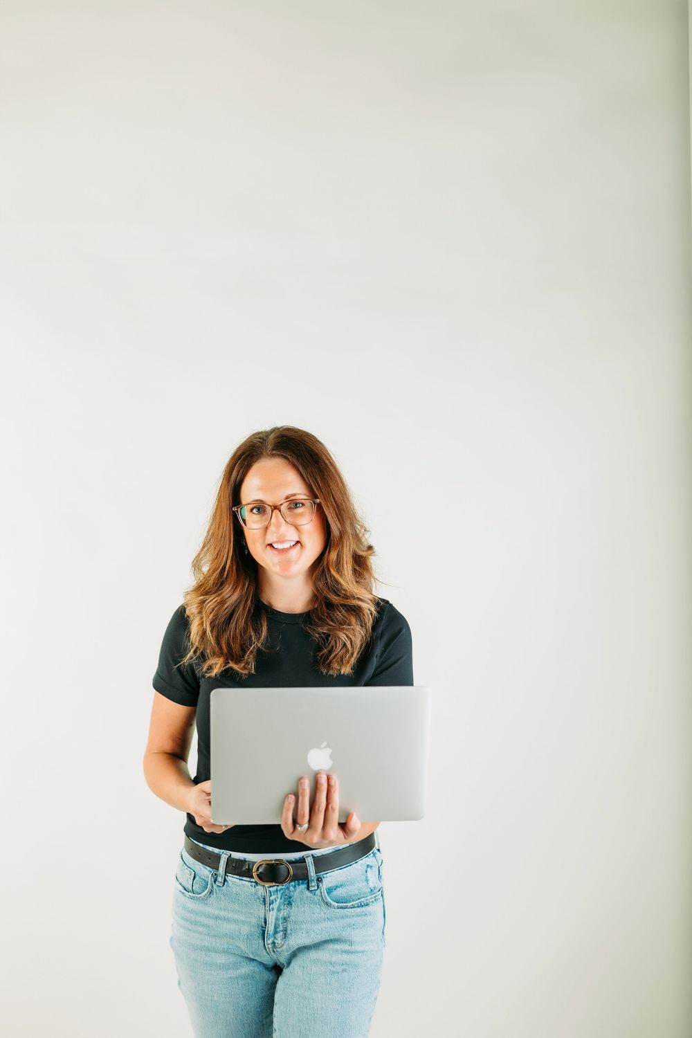 Professional working on MacBook laptop in casual attire against white background with joyful expression.