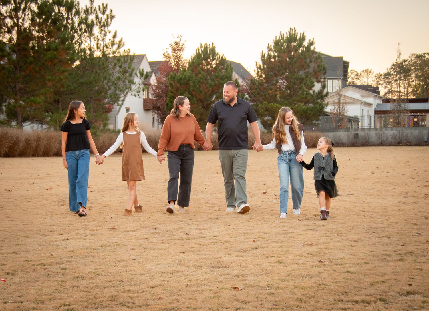 A family walking hand in hand across an open field at sunset.