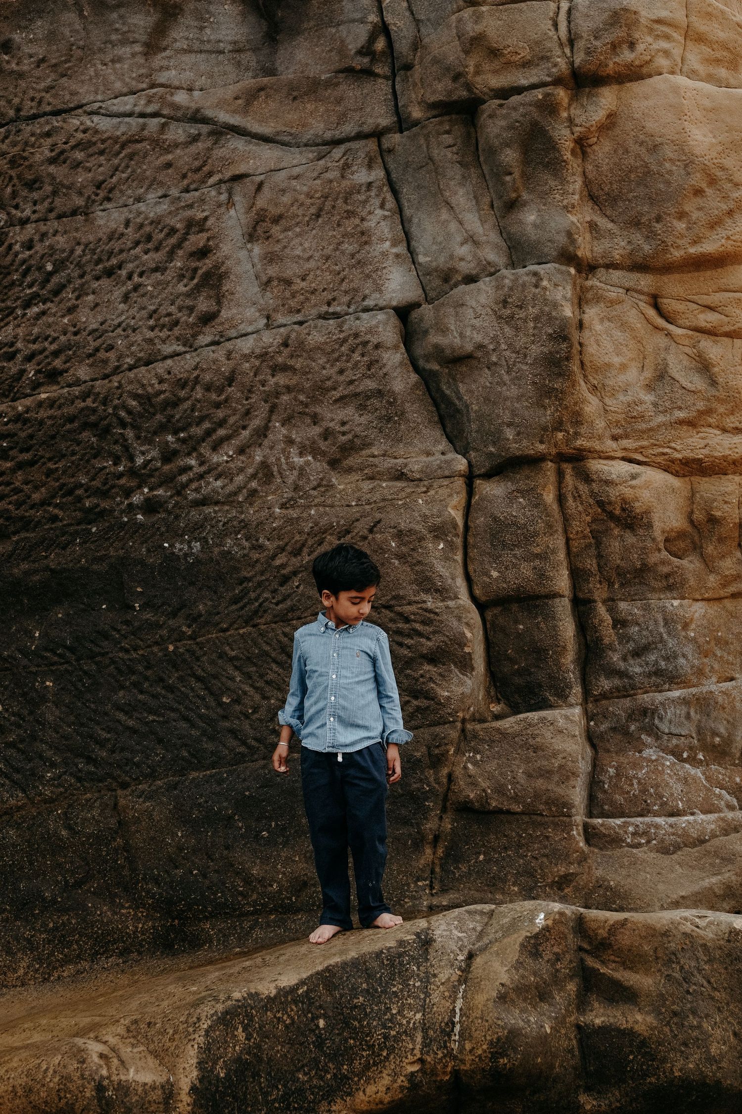 Young child standing against natural rock formations during an outdoor lifestyle family photography session in Northumberland, Bamburgh Beac