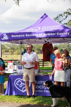 Humane Society of Sumter County booth at outdoor event with purple tent and display table.