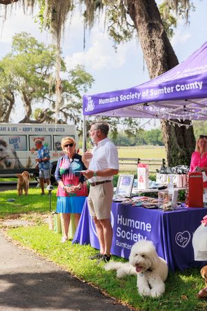 Humane Society booth setup at outdoor event with purple tent and display tables.