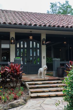 Spanish-style building exterior with tiled roof, stone steps, and decorative landscaping.