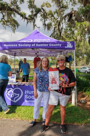 Humane Society volunteers standing under purple tent at community outreach event.