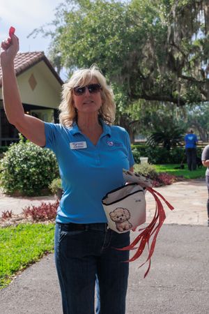 Humane Society volunteer in blue polo shirt waving while holding leashes at outdoor event.