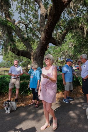 Group gathered under large oak trees draped with Spanish moss on a sunny day.
