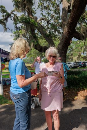 Attendees interact at an outdoor event under large oak trees with Spanish moss.