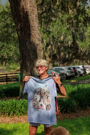 Person holding up decorative t-shirt with dog design outdoors.