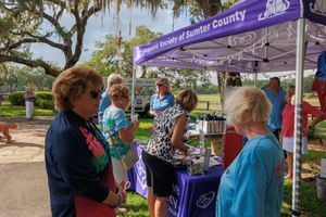 People gather under a purple Humane Society tent at an outdoor community event.