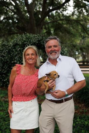 Small brown dog being held at outdoor adoption event.