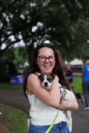 A person in a white top hugs and smiles with a small black and white puppy outdoors.