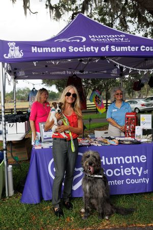 Purple Humane Society tents display information while volunteers engage with visitors at a community event.