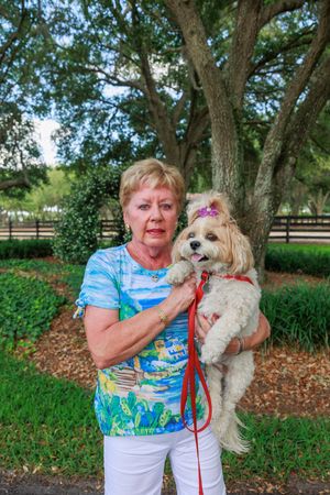 Small white fluffy dog on red leash enjoying outdoor park setting.