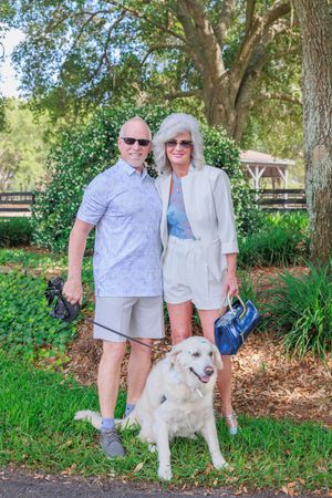 White fluffy dog posing with owners under shaded trees.