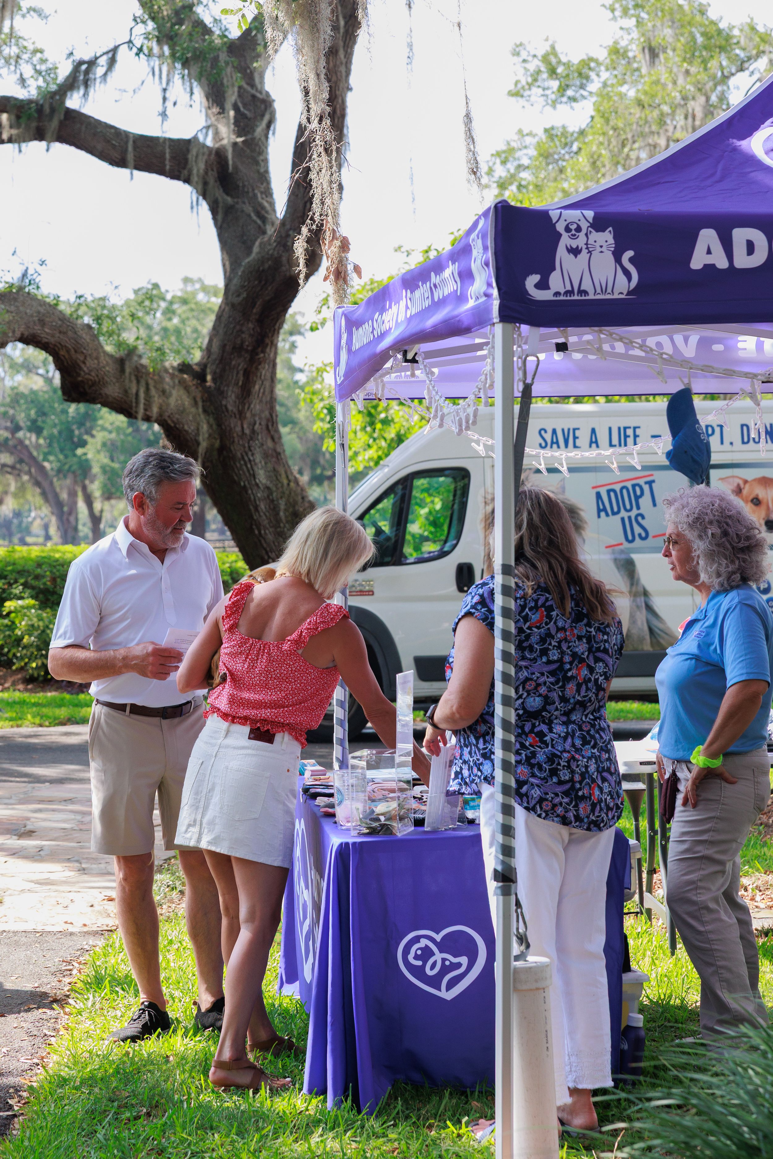 People gather at outdoor information booths with purple canopies at a community event.