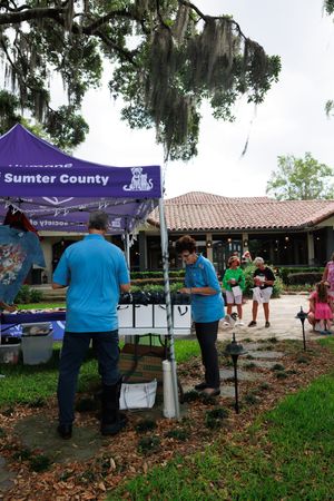 Purple tent and display setup for Sumter County Humane Society event under shaded trees.