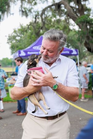 Person in white shirt holding and feeding a small rescue puppy at adoption event.