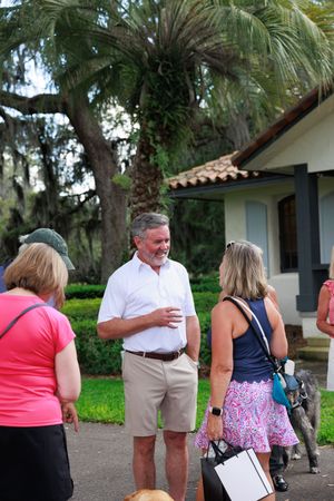 Attendees interact at outdoor community event with Spanish moss trees in background.