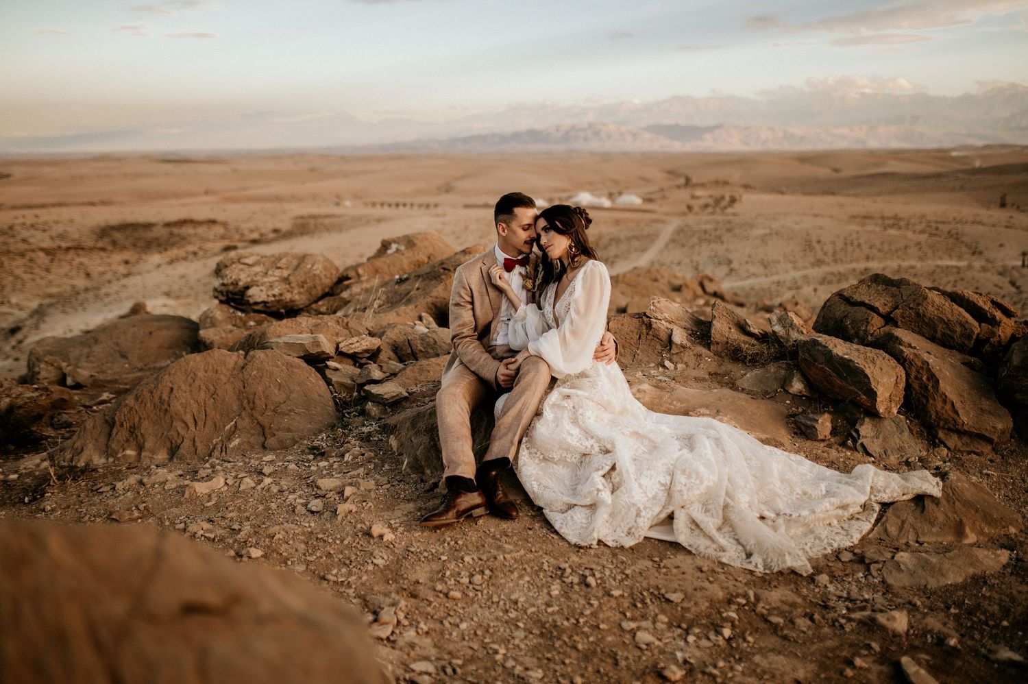 Couple in wedding attire photographed along desert cliffs in warm sepia tones.