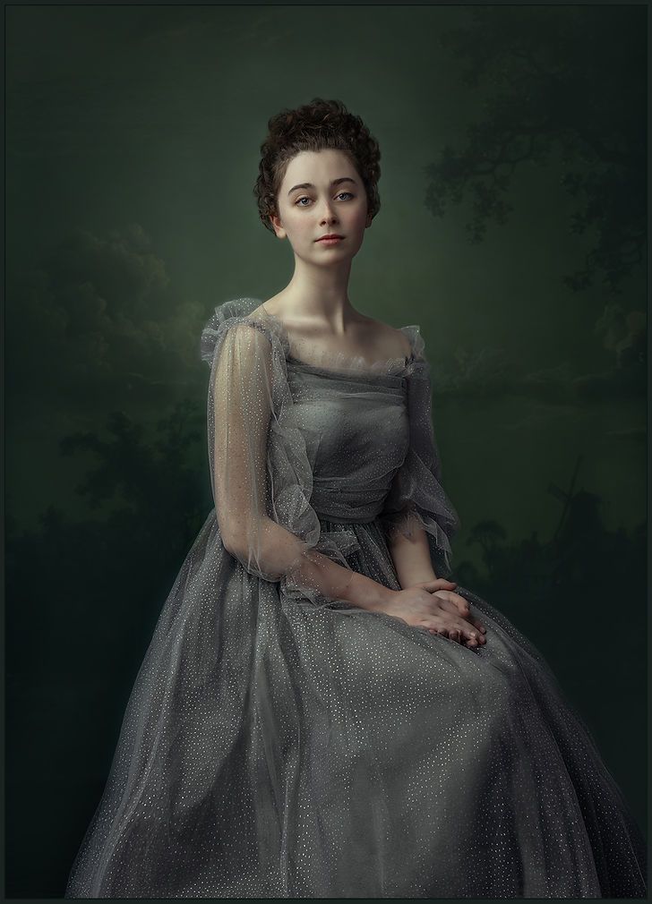 Young woman in elegant silver-grey tulle gown seated gracefully against a dark green painterly background.