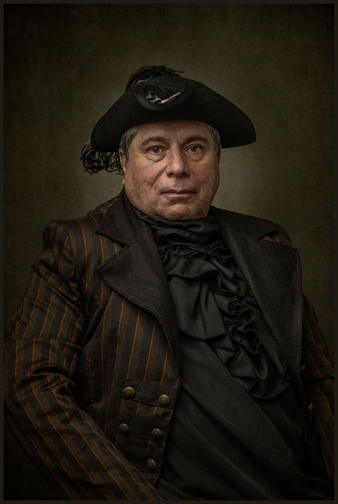 Middle-aged man in period tricorn hat and striped coat in a dramatic old master portrait style.