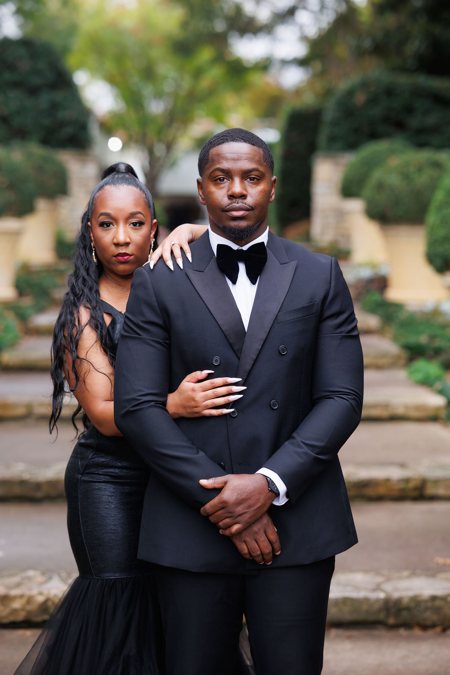A couple in white outfits share a romantic moment in a garden setting during a photoshoot.