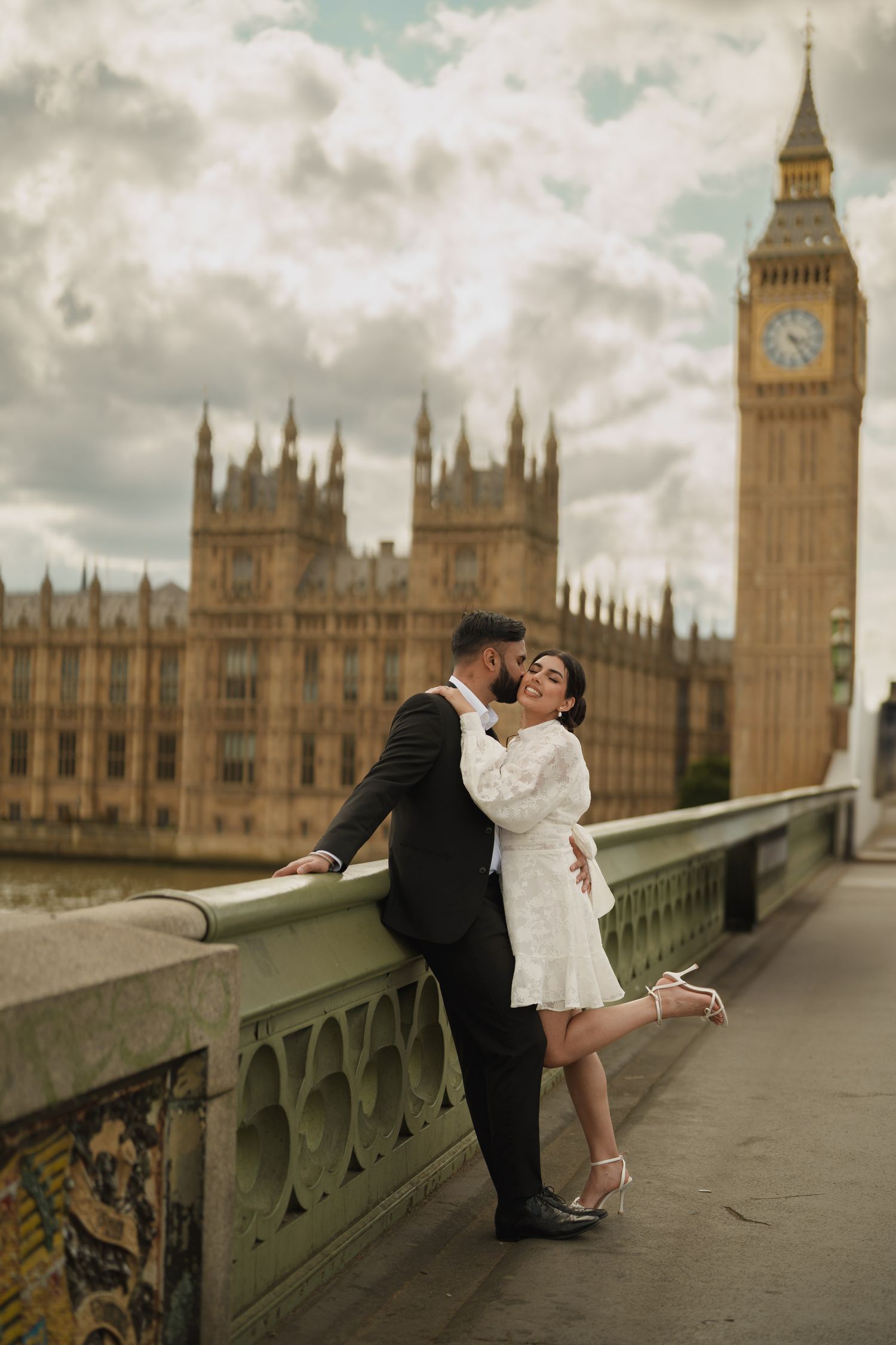 A romantic couple in formal attire pose on Westminster Bridge with Big Ben and Parliament in the background in London.
