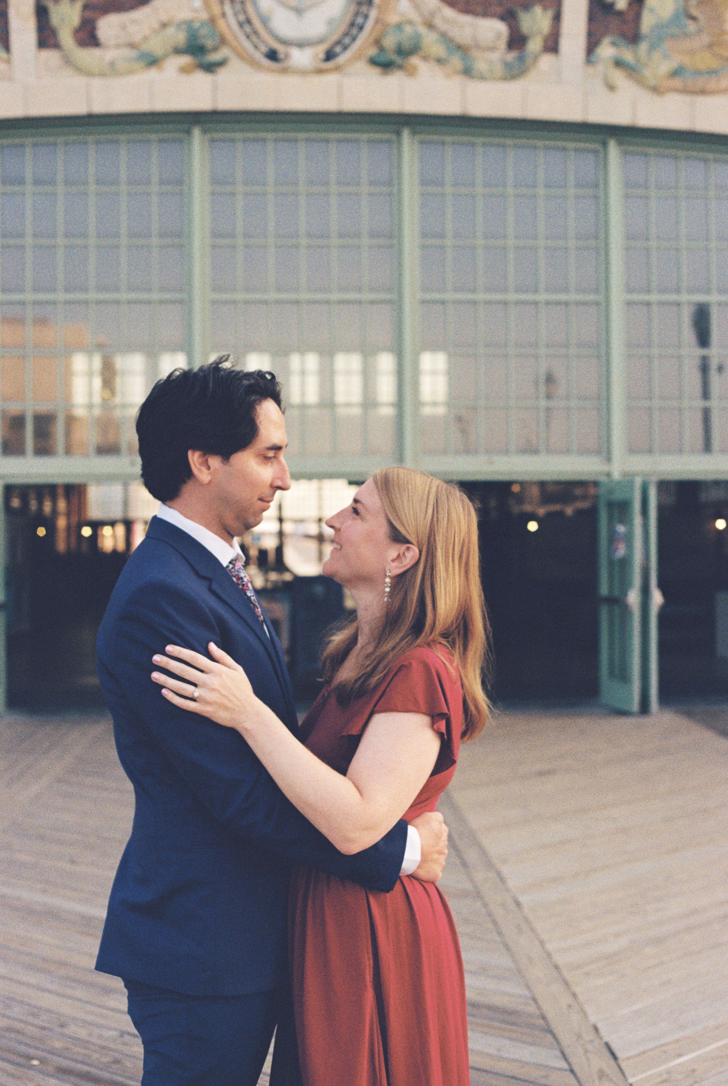 A couple in formal attire share a romantic moment outside an ornate building with vintage architecture.