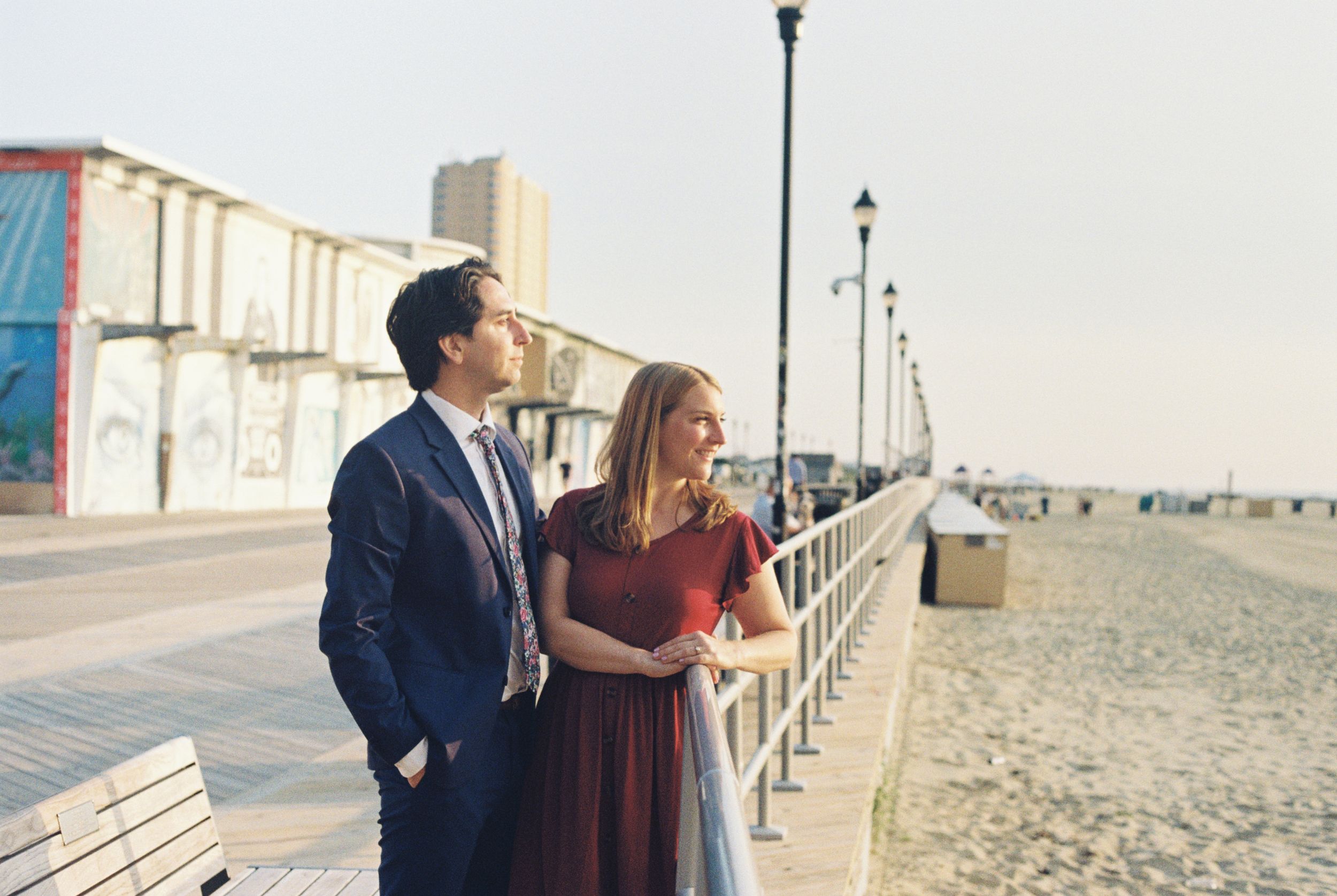 A couple stands together on a beach boardwalk during a cloudy day, with storage containers visible in the background.