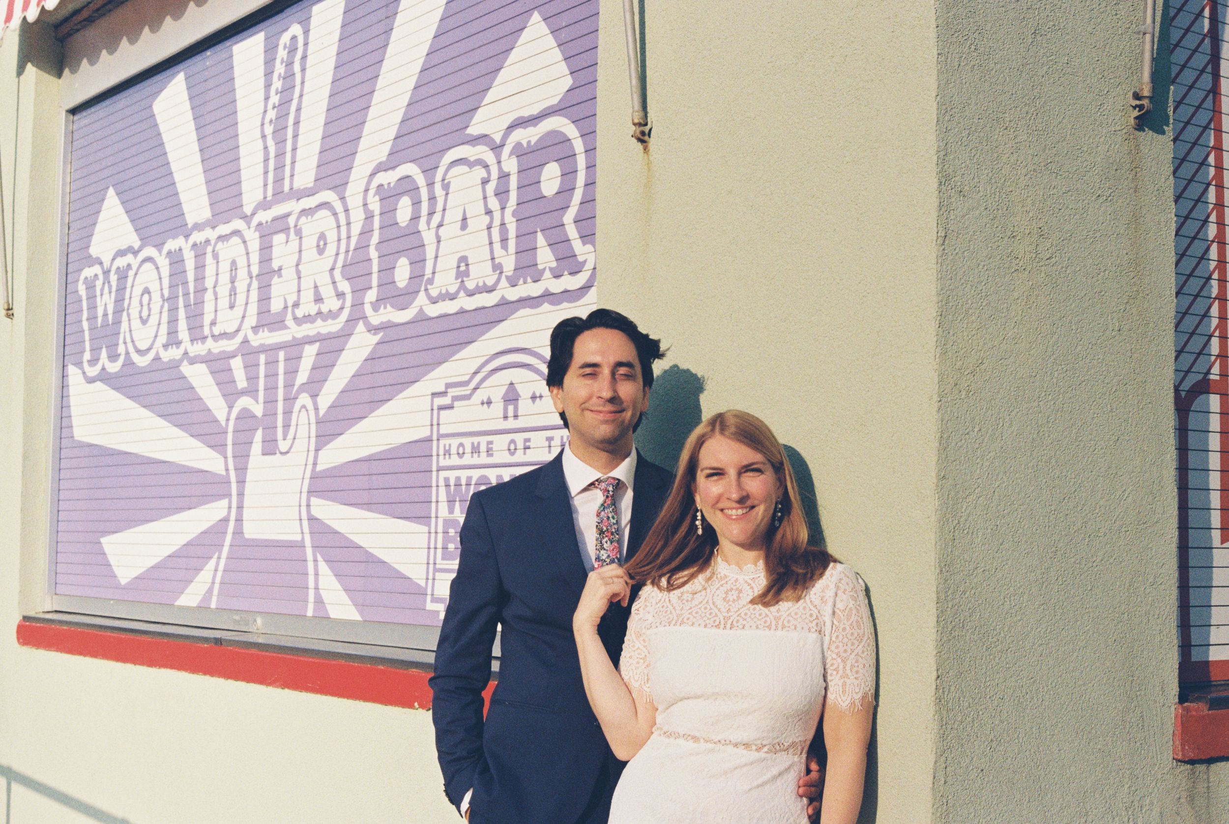 A group of people stand in front of a purple and white wall with retro-style graphics and signage.