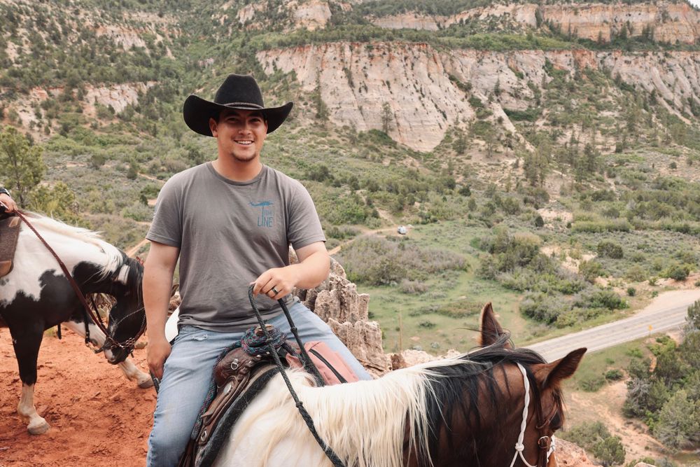 Group of horses and riders on a trail in a scenic red rock canyon.
