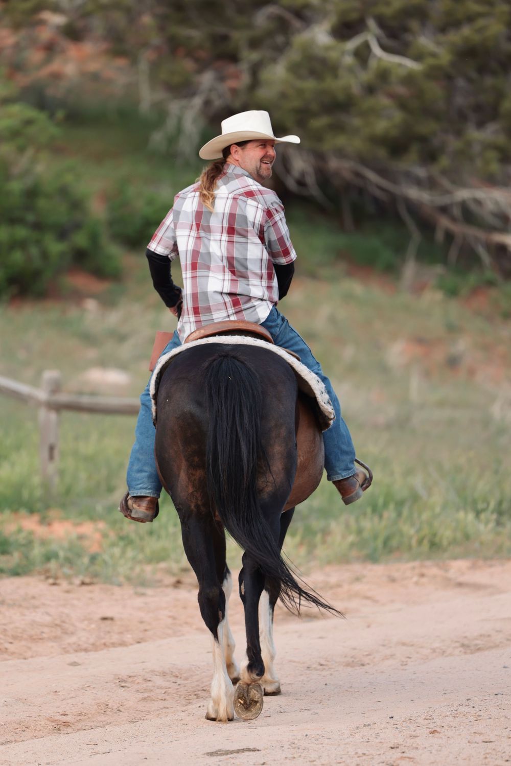 Horseback rider in cowboy attire traveling down a dirt path.