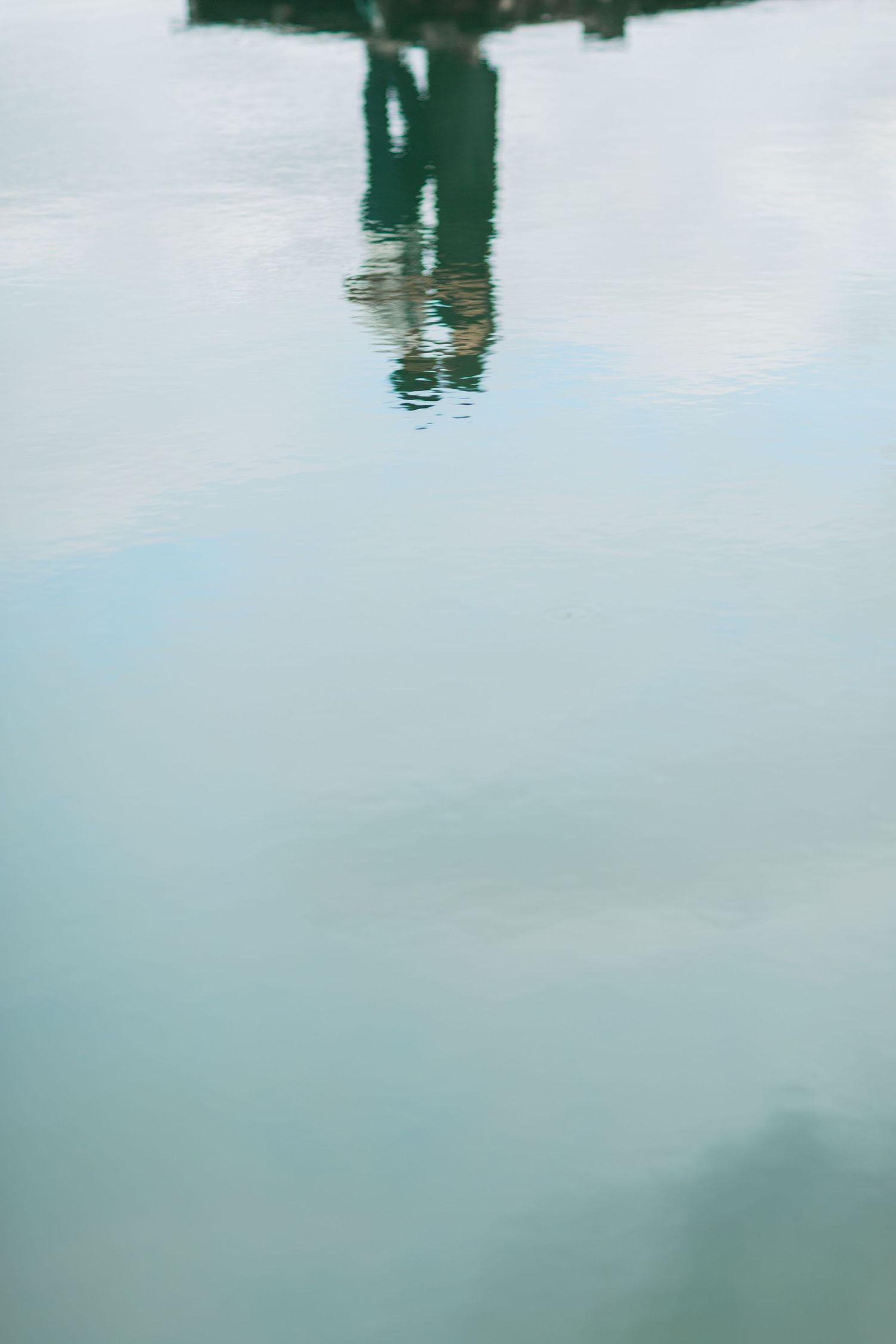 A couple's reflection appears in calm water creating a mirror-like effect with ripples and a blue-tinted surface proposal photographer