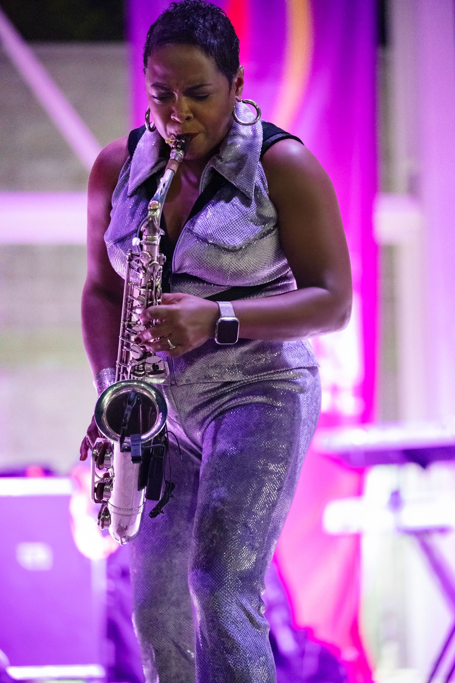 Musician performs passionately on saxophone against vibrant purple and pink stage lighting during live performance.