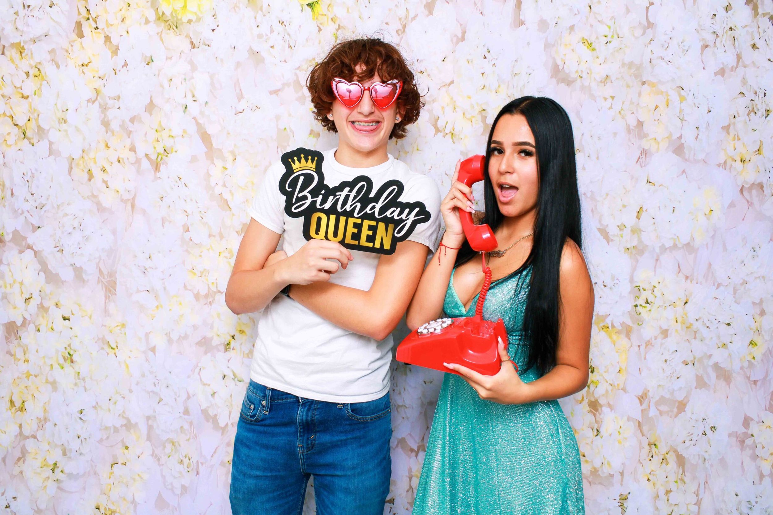 A group of friends poses playfully with party props and colorful outfits against a sparkly gold backdrop.