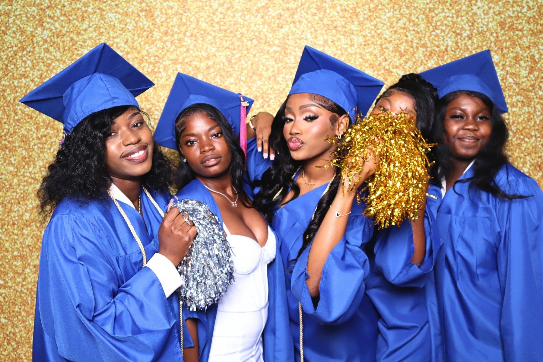 A group of graduates in bright blue caps and gowns pose together with gold pom poms against a sparkly backdrop.