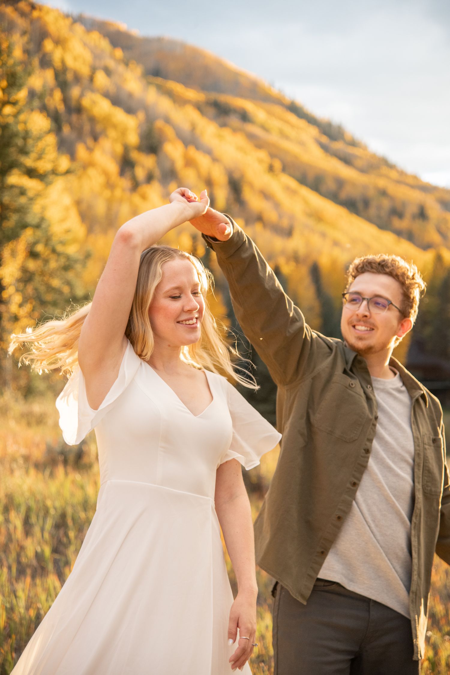 A couple dances joyfully together against a backdrop of golden autumn mountains at sunset engagement photos in Vail Colorado