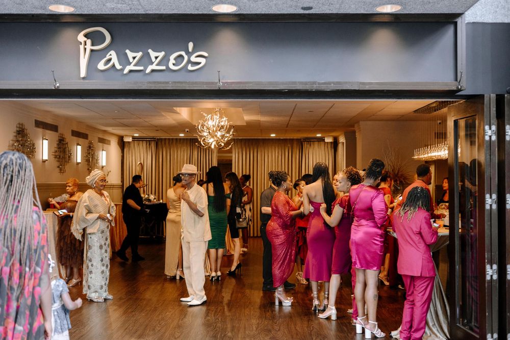 Wedding party in formal attire dancing and celebrating in a reception hall with Pazzo's signage visible.