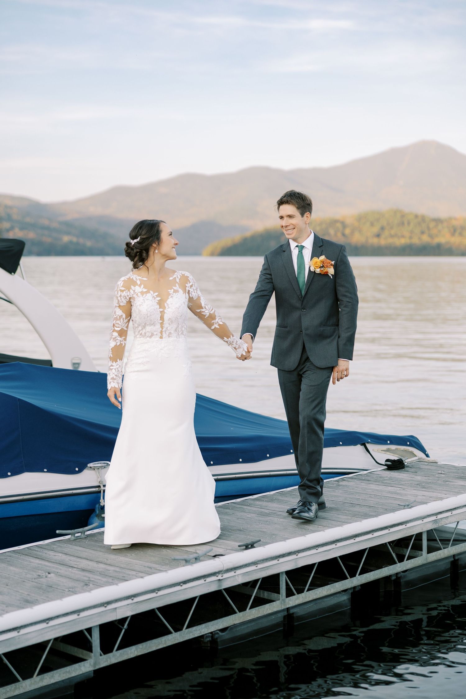 A couple in wedding attire shares a romantic moment on a wooden dock by Lake Placid with the Adirondack mountains in the background.