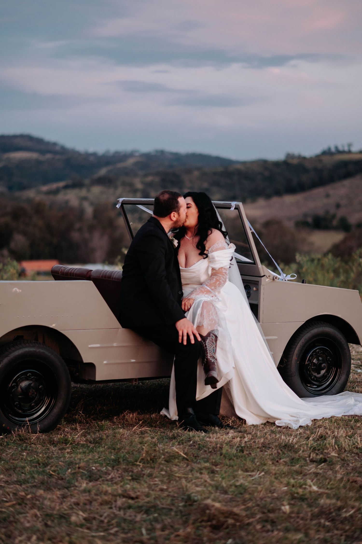 A romantic wedding photo series shows a couple sitting together by a vintage car in a rustic outdoor setting at sunset.