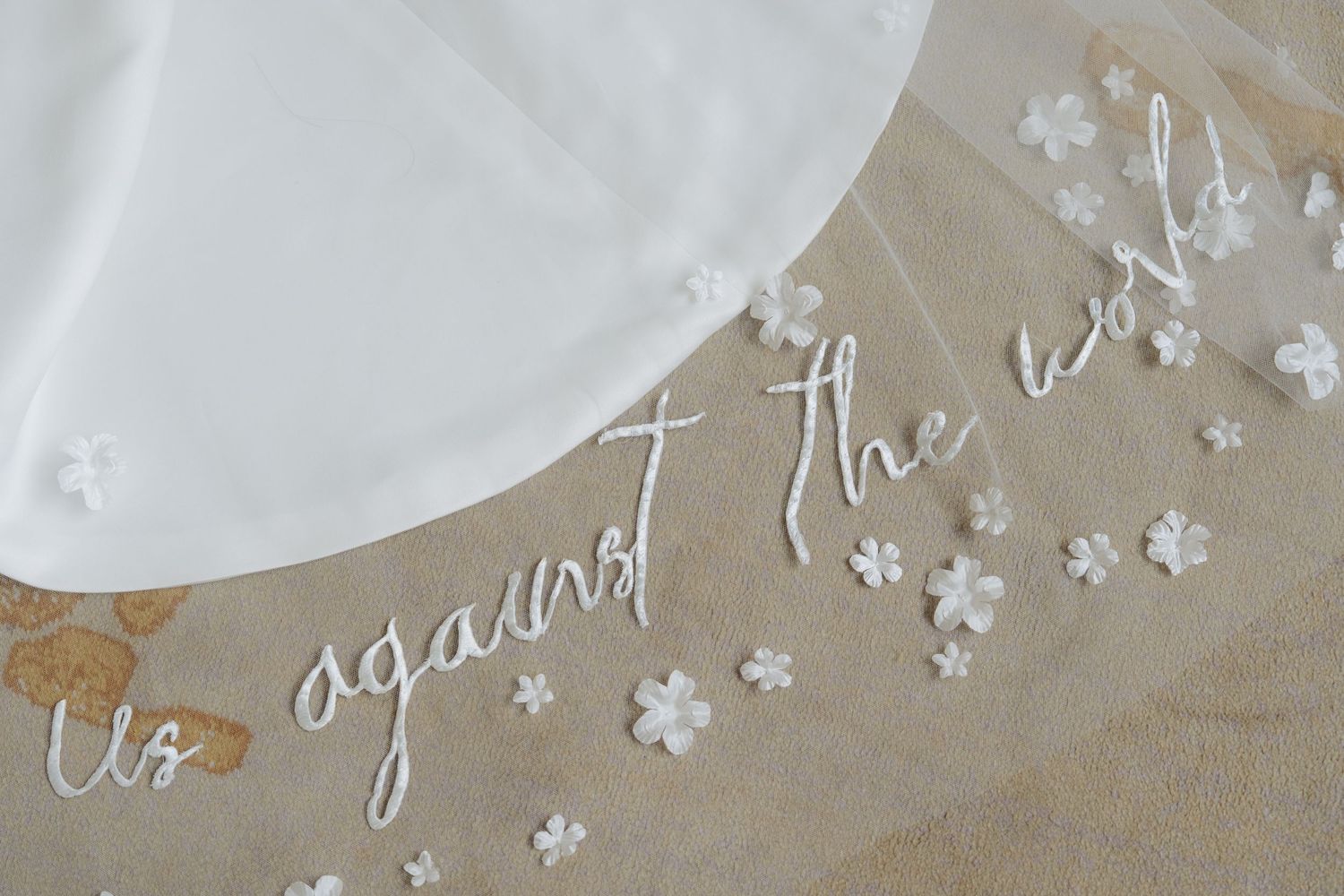 Elegant wedding veil with embroidered text reading us against the world adorned with delicate white floral appliques.