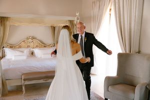 A wedding dress hangs elegantly in a bright white bridal suite with ornate vintage furniture.