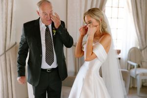 A wedding first look moment captured in an elegant room with white curtains and natural light streaming in.
