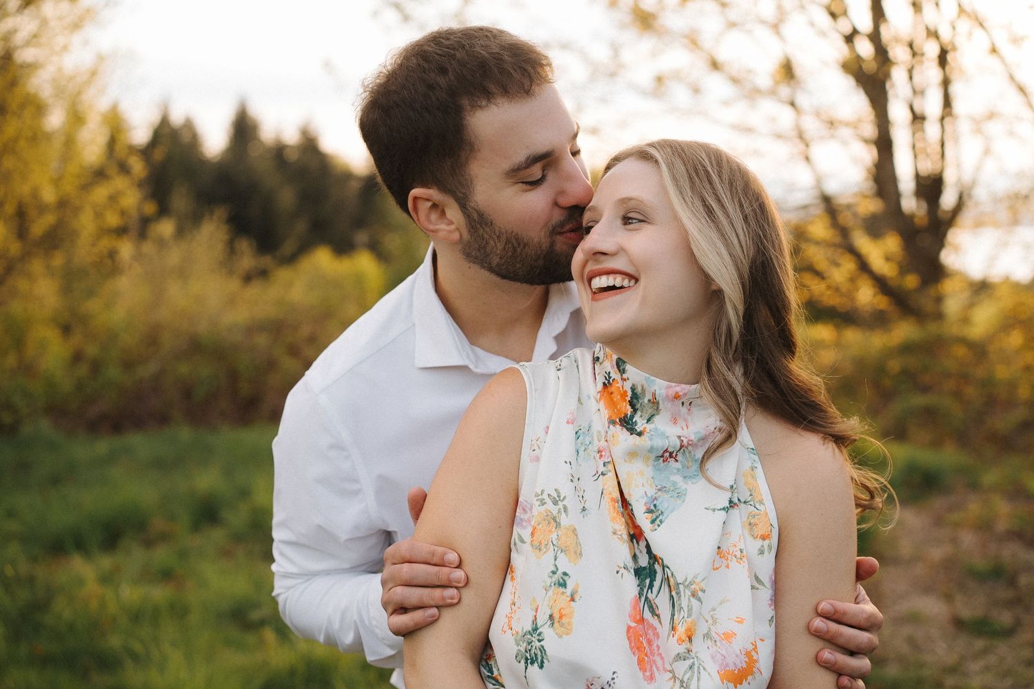 Romantic couple embraces in golden autumn sunlight during outdoor photoshoot.
