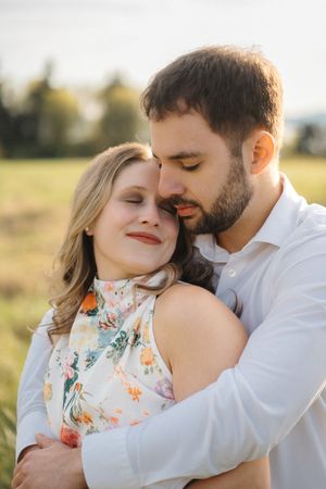 A romantic couple embraces in a sunlit field wearing white and floral clothing during an intimate photoshoot.