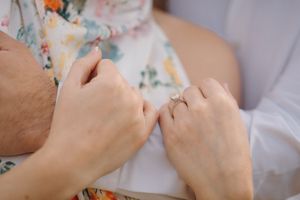 Close up view of hands embroidering colorful floral patterns on white fabric using needle and thread.