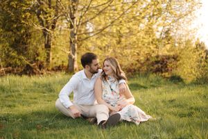 A couple sits together on grassy hill during golden hour autumn photoshoot in a park.